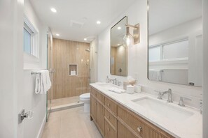 A modern bathroom with a large mirror, two sinks, a shower, and a toilet. - Luxury Oceanfront Retreat w/ Hot Tub, Fire Table & Pacific Views near S.F. (Moss Beach)