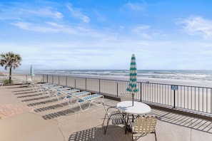 Eine Strandterrasse mit Liegestühlen, einem Tisch und einem Sonnenschirm mit Blick auf das Meer.