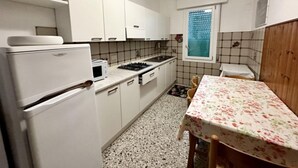 Ett kompakt kök med vita skåp, en spis, ett handfat och ett bord med ett blommigt bordsduk.