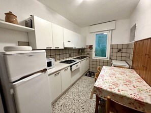 Eine kompakte Küche mit weißen Schränken, einem Herd, einer Spüle und einem Tisch mit einer blumigen Tischdecke.