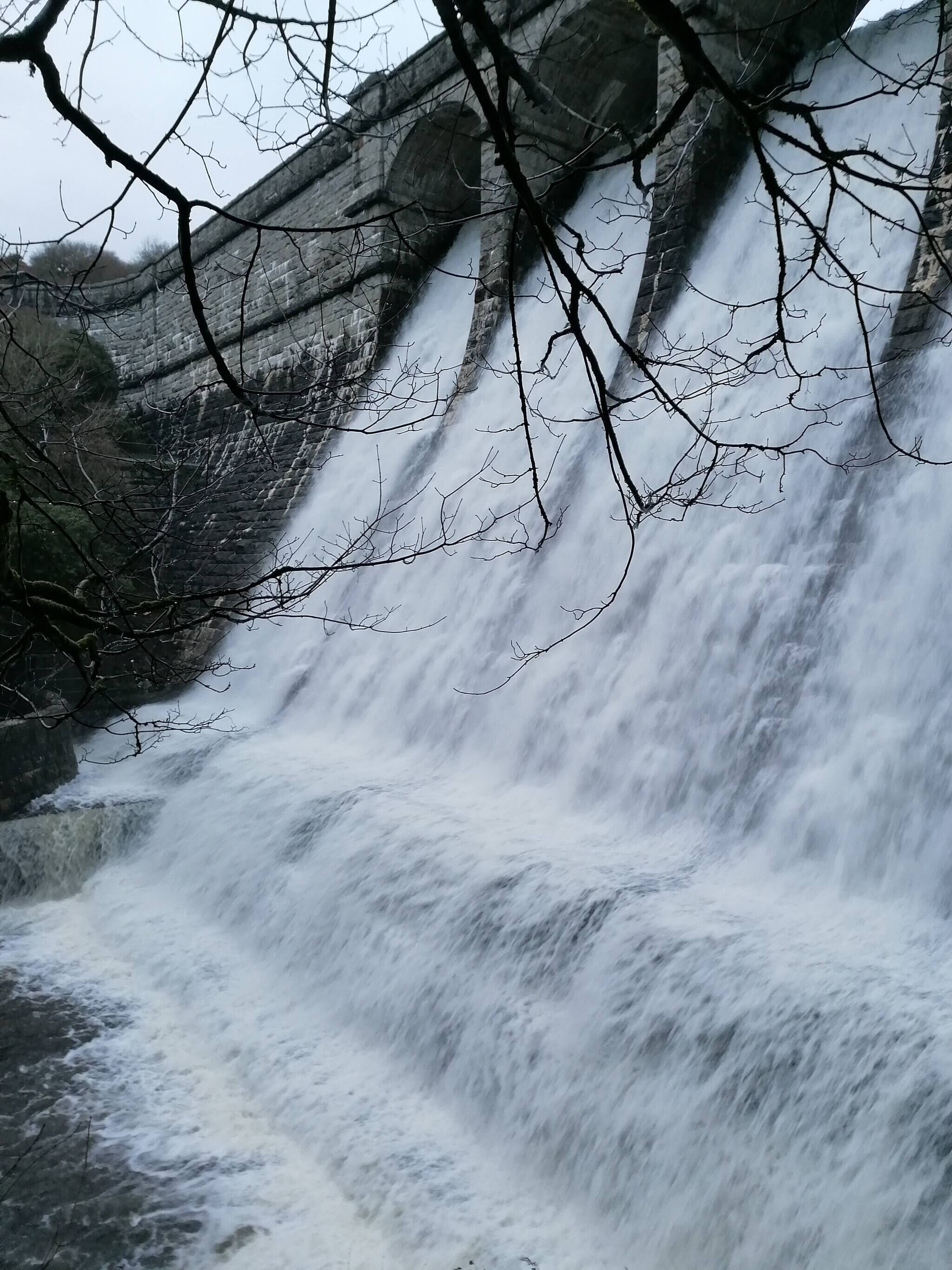 A waterfall cascading over a stone structure with bare branches overhead.