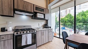 A modern kitchen with a gas stove, microwave, and built-in oven, large windows with a view of the city, and a dining area with a table and chairs. - Group-Friendly 3BR in Roma Norte (Ciudad de México)