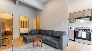 A modern living room with a grey sectional sofa, a small wooden coffee table, and a kitchen area with a stove and cabinets. - Group-Friendly 3BR in Roma Norte (Ciudad de México)
