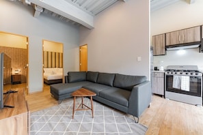 A modern living room with a grey sectional sofa, a small wooden coffee table, and a kitchen area with a stove and cabinets. - Group-Friendly 3BR in Roma Norte (Ciudad de México)