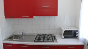 A kitchen with red cabinets, a white countertop, a gas stove, a sink, and a microwave. - Functional Stay for Five Guests in Bibione (San Michele al Tagliamento)