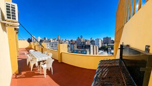 Terraço no telhado com uma mesa, cadeiras, um piano e vista da cidade.