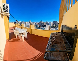 Eine Dachterrasse mit Tisch, Stühlen, einem Klavier und Blick auf die Stadt.