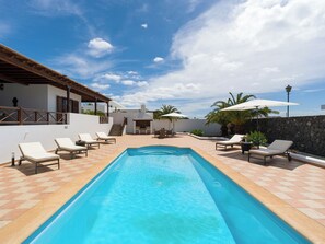 A swimming pool with lounge chairs, a stone wall, and a building with a balcony. - Villa with private swimming pool in Puerto Calero, Lanzarote (Puerto Calero)