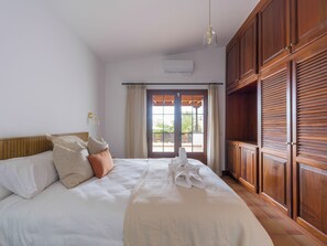 A bedroom with a bed, a wooden wardrobe, a window with curtains, and an air conditioning unit. - Villa with private swimming pool in Puerto Calero, Lanzarote (Puerto Calero)