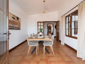 A dining area with a long table, chairs, and a kitchen in the background. - Villa with private swimming pool in Puerto Calero, Lanzarote (Puerto Calero)