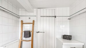 Une salle de bain avec des carreaux blancs, une échelle en bois, un porte-serviettes, un radiateur et un petit meuble blanc avec un panier.