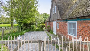 Une maison traditionnelle à toit de chaume, avec une allée en gravier et une clôture en bois.