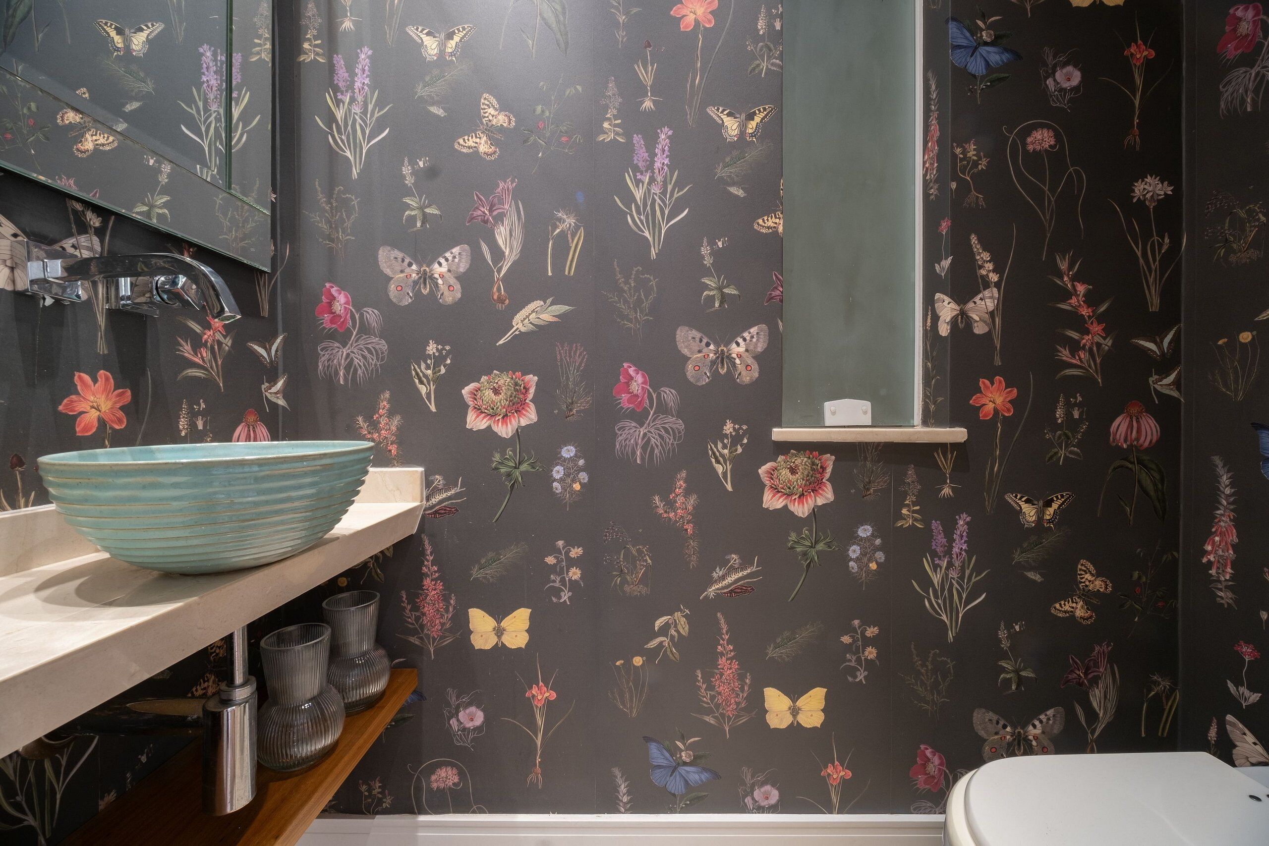 Et badeværelse med blomstret tapet, en blå skål på vasken og et toilet.