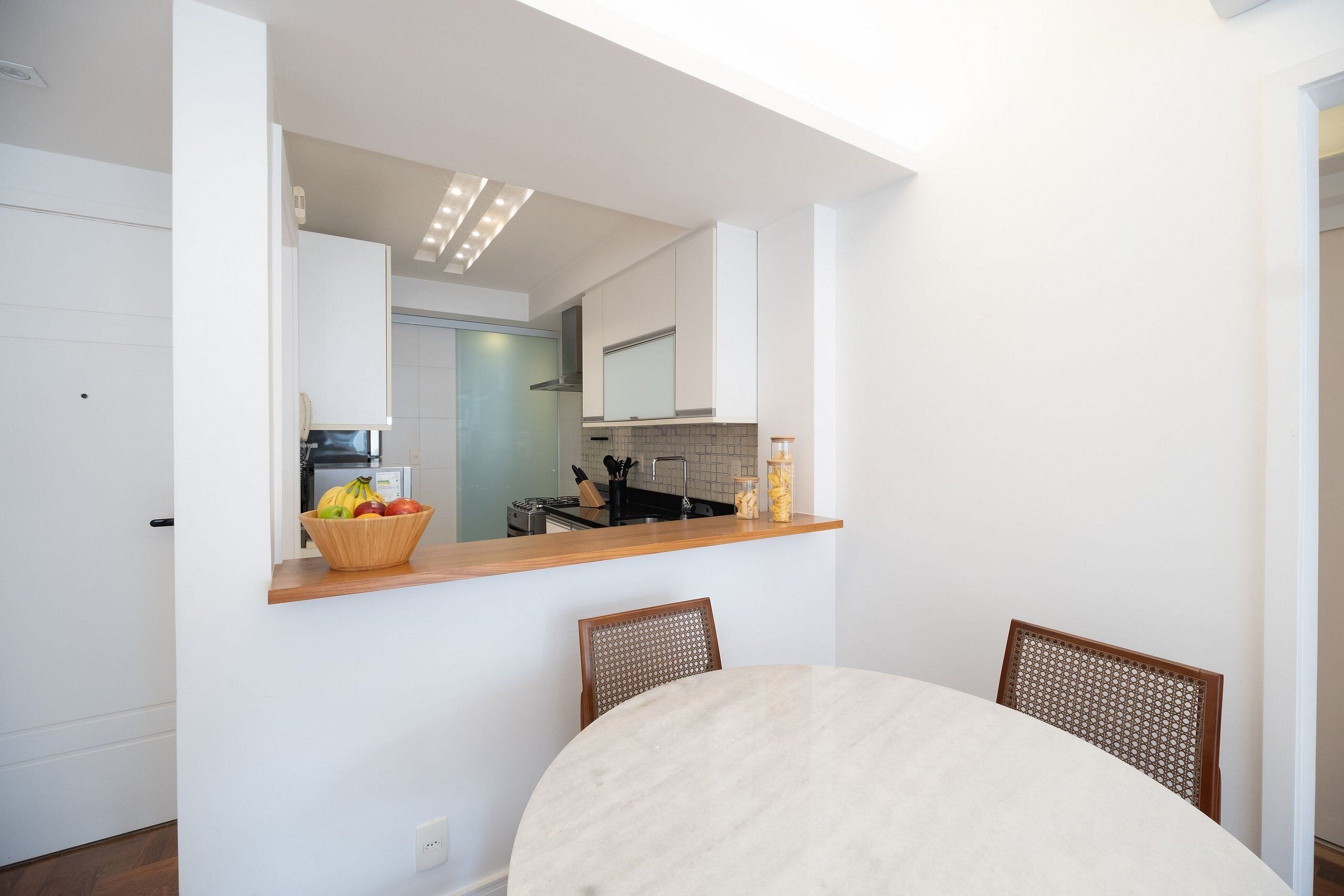 A modern kitchen with a wooden countertop, a dining table with chairs, and a view into the adjacent living area.