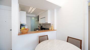 A modern kitchen with a wooden countertop, a dining table with chairs, and a view into the adjacent living area.