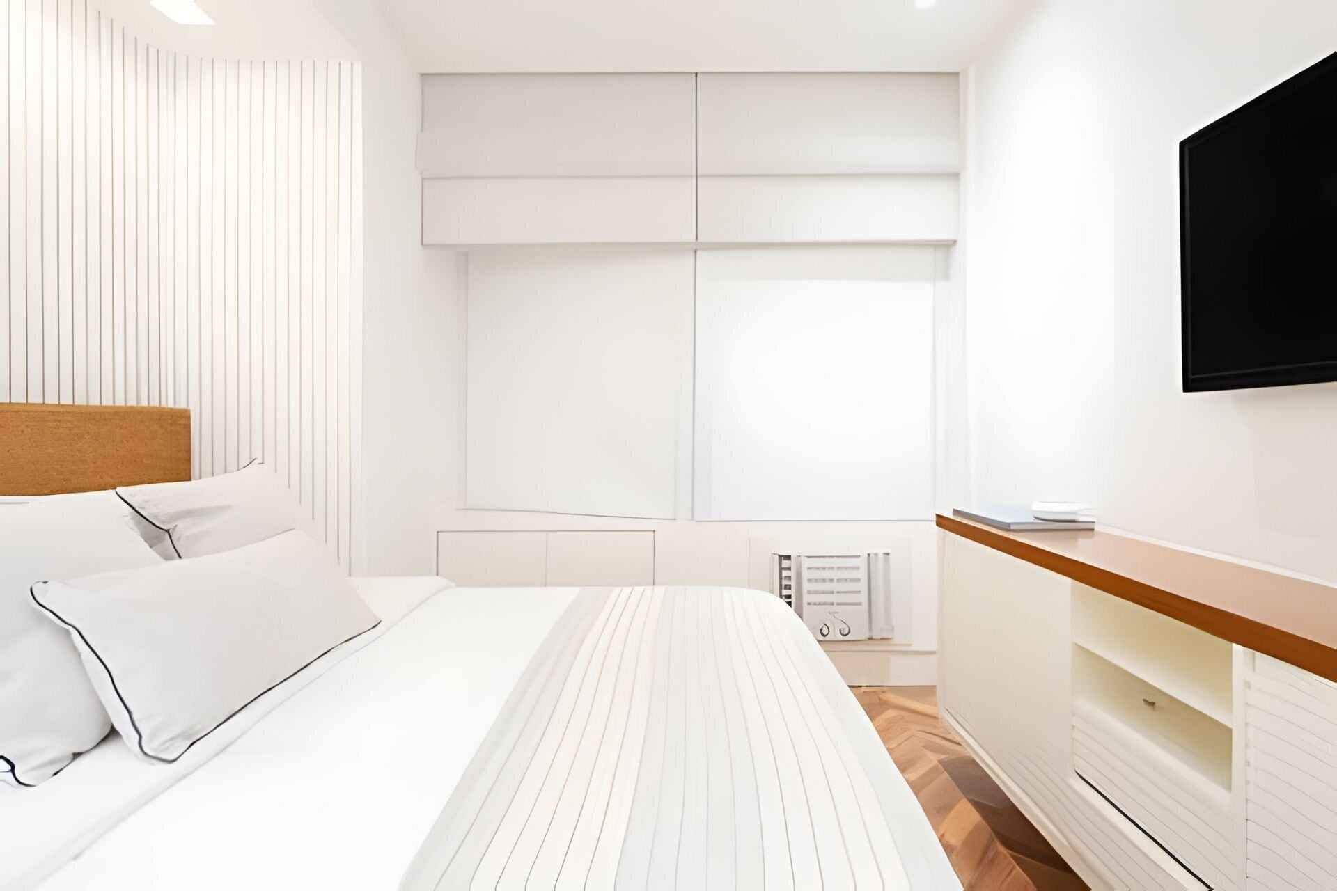A modern bedroom with a bed, a TV, a bedside table, and a radiator.