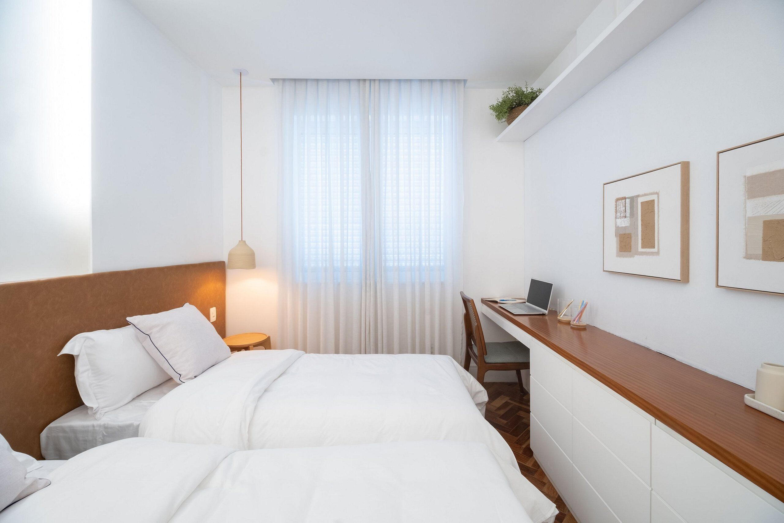 A hotel room with a bed, a desk, a chair, a lamp, and framed pictures on the wall.