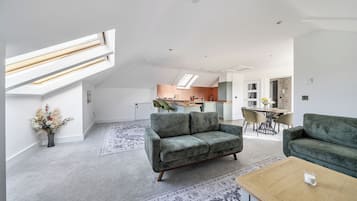 En rummelig opholdsstue med højt til loftet, ovenlysvindue og et moderne køkken i baggrunden.