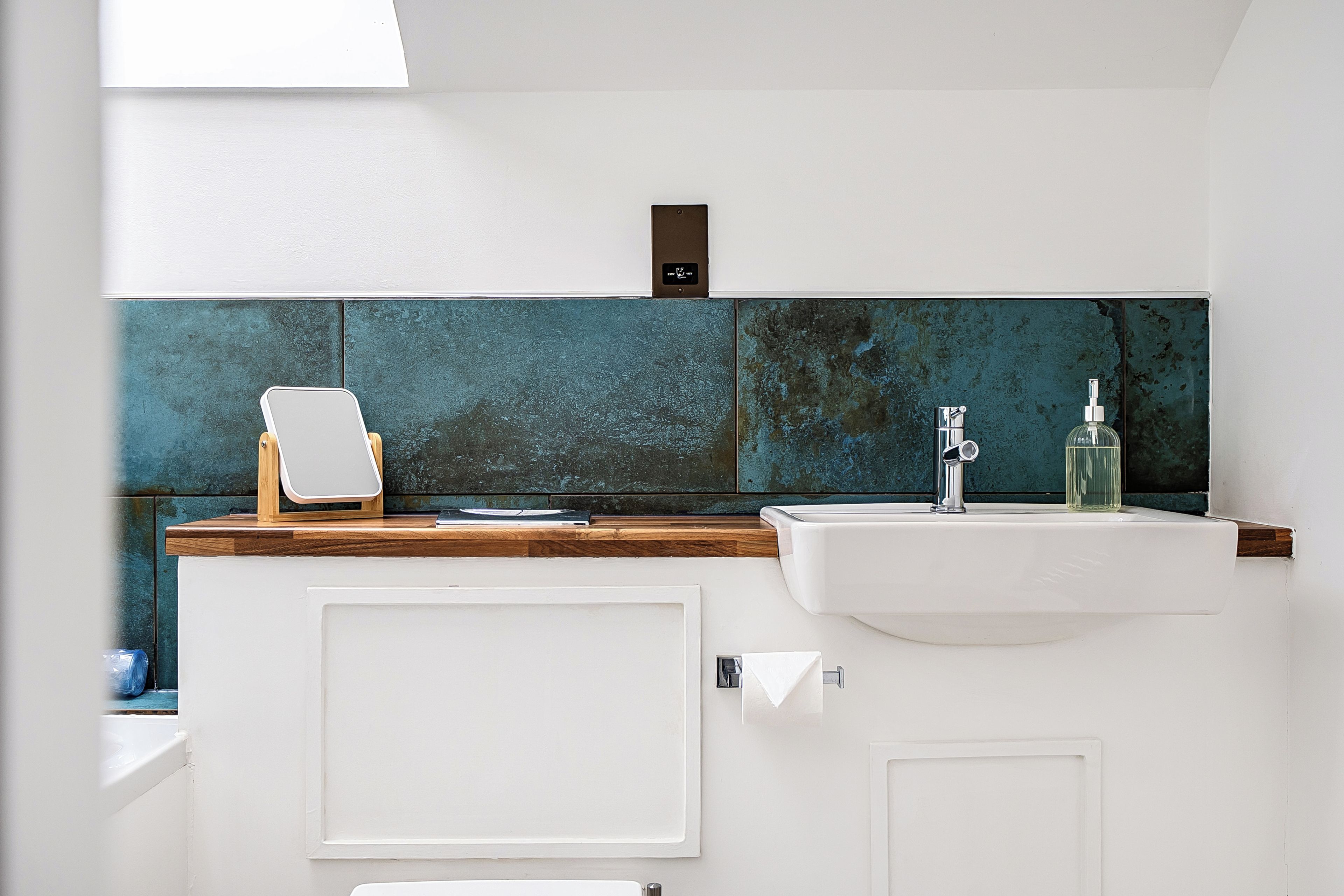 A bathroom with a white sink, a mirror, and a blue-tiled backsplash.