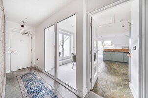 A hallway with a patterned rug, a white door, and a view into a dining area with a table and chairs.