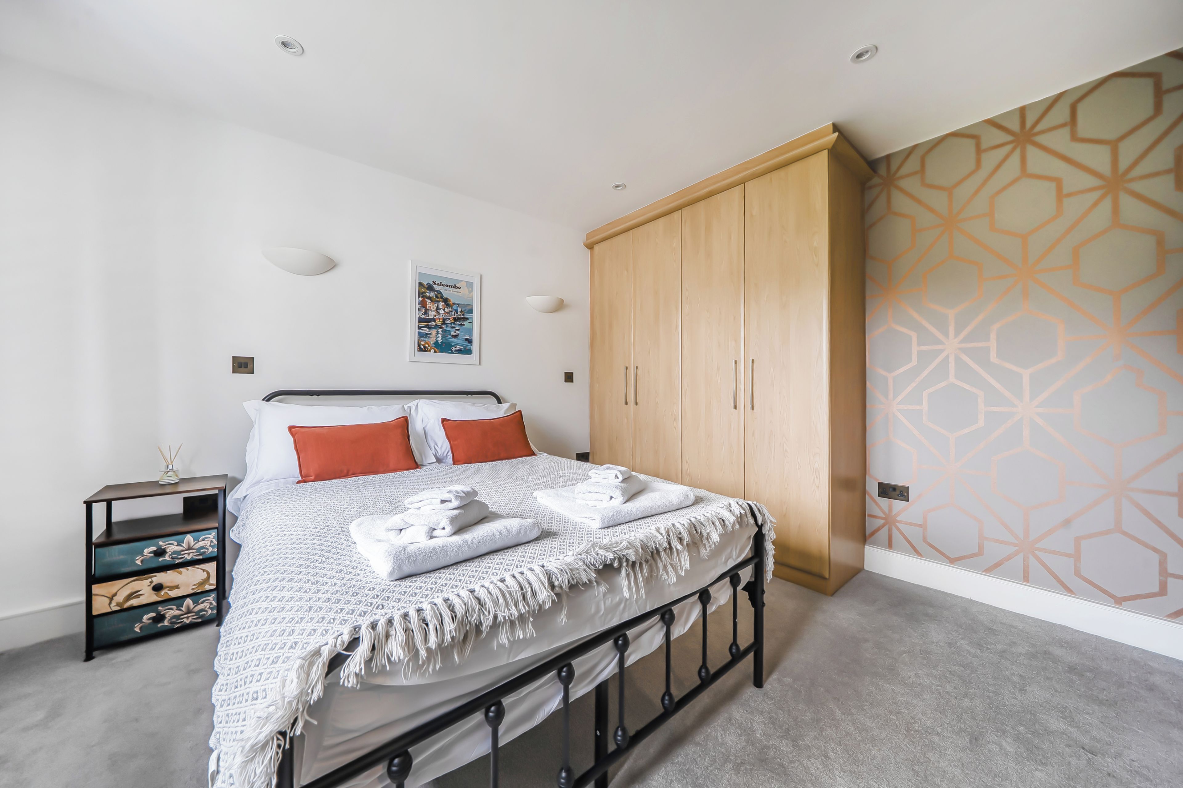 Une chambre à coucher comprenant un lit, une armoire, une table de chevet et un mur orné d’un motif géométrique.