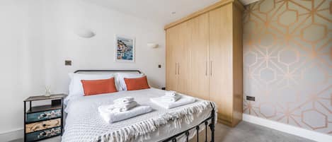 A bedroom with a bed, a wardrobe, a nightstand, and a wall with a geometric pattern.