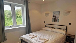 A bedroom with a bed, a window, a painting, and a bedside table. - Apartment Sleeps 4 With Balcony and Parking (Kingsbridge)