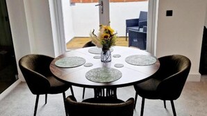 A round table with a vase of flowers, two chairs, and a view of a garden through a glass door. - Apartment Sleeps 4 With Balcony and Parking (Kingsbridge)