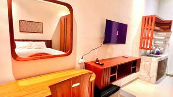 Una habitación de hotel moderna con un espejo grande, un televisor montado en la pared, un escritorio de madera y una zona de cocina integrada.