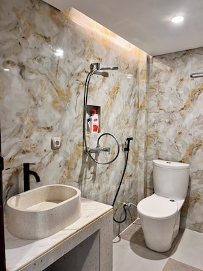 A bathroom with a marble wall, a round sink, a toilet, and a shower head. - Diafragma Livin (Nusa Dua)