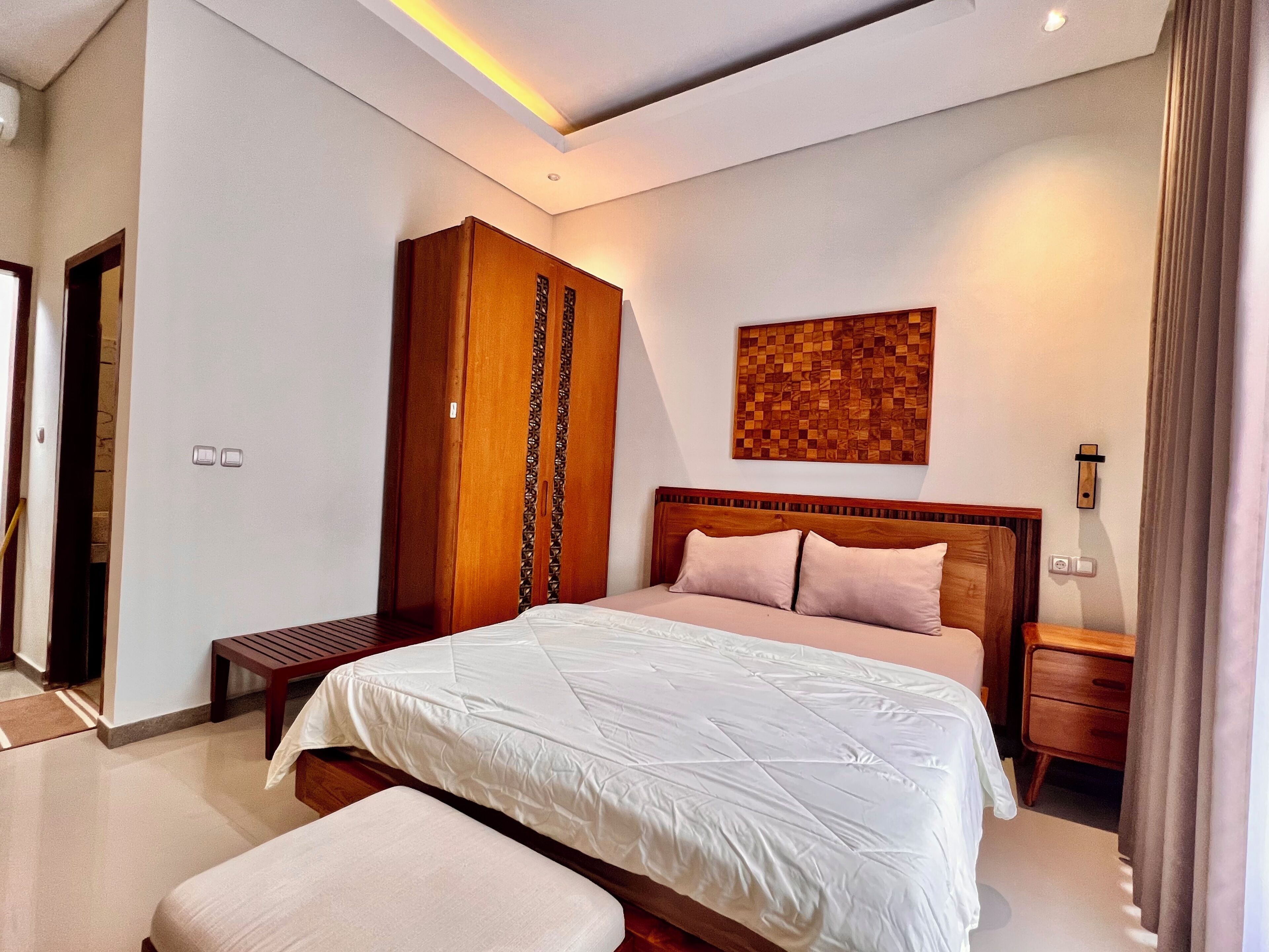 Une chambre à coucher moderne avec un grand lit, une armoire en bois, une petite table de chevet et une œuvre d’art accrochée au mur.