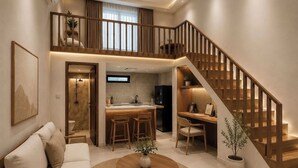 A spacious living area with a sofa, a dining table, a kitchen with a bar, and a wooden staircase. - Diafragma Livin (Nusa Dua)