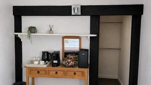 Habitación de hotel con escritorio de madera, cafetera, parlante, espejo y estante con planta y florero pequeño.