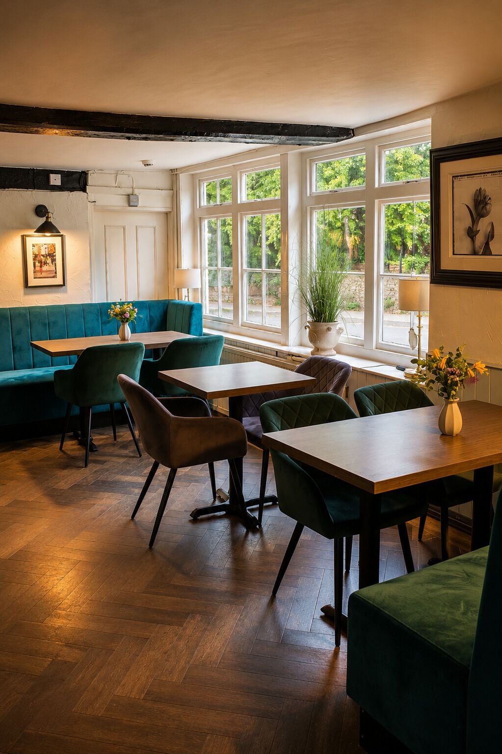 A dining area with wooden tables and chairs, a teal booth, and large windows with a view of greenery.