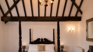 Una cama con dosel y tablero de madera, una mesita de noche con lámpara, un aparador con lámpara, un tocador de madera y un espejo en la pared.
