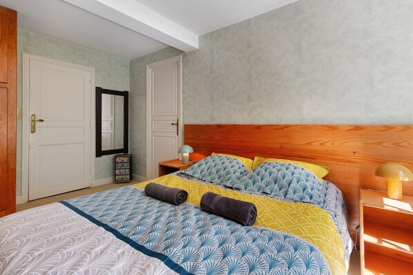 A bedroom with a bed, wooden headboard, two nightstands, a mirror, and a wardrobe.