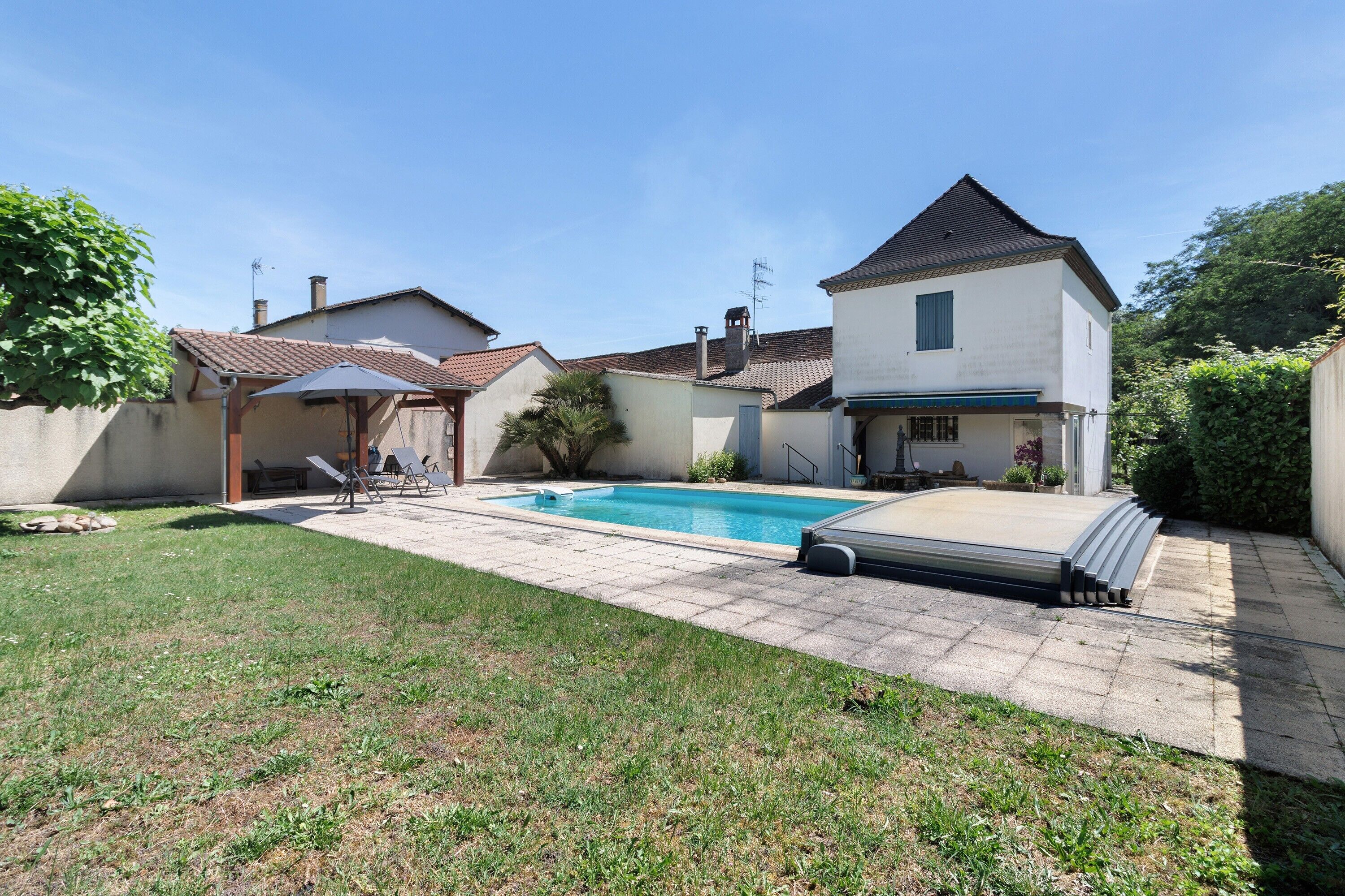 Un jardin à l’arrière d’une maison, avec une piscine, un patio couvert et une maison à deux étages.