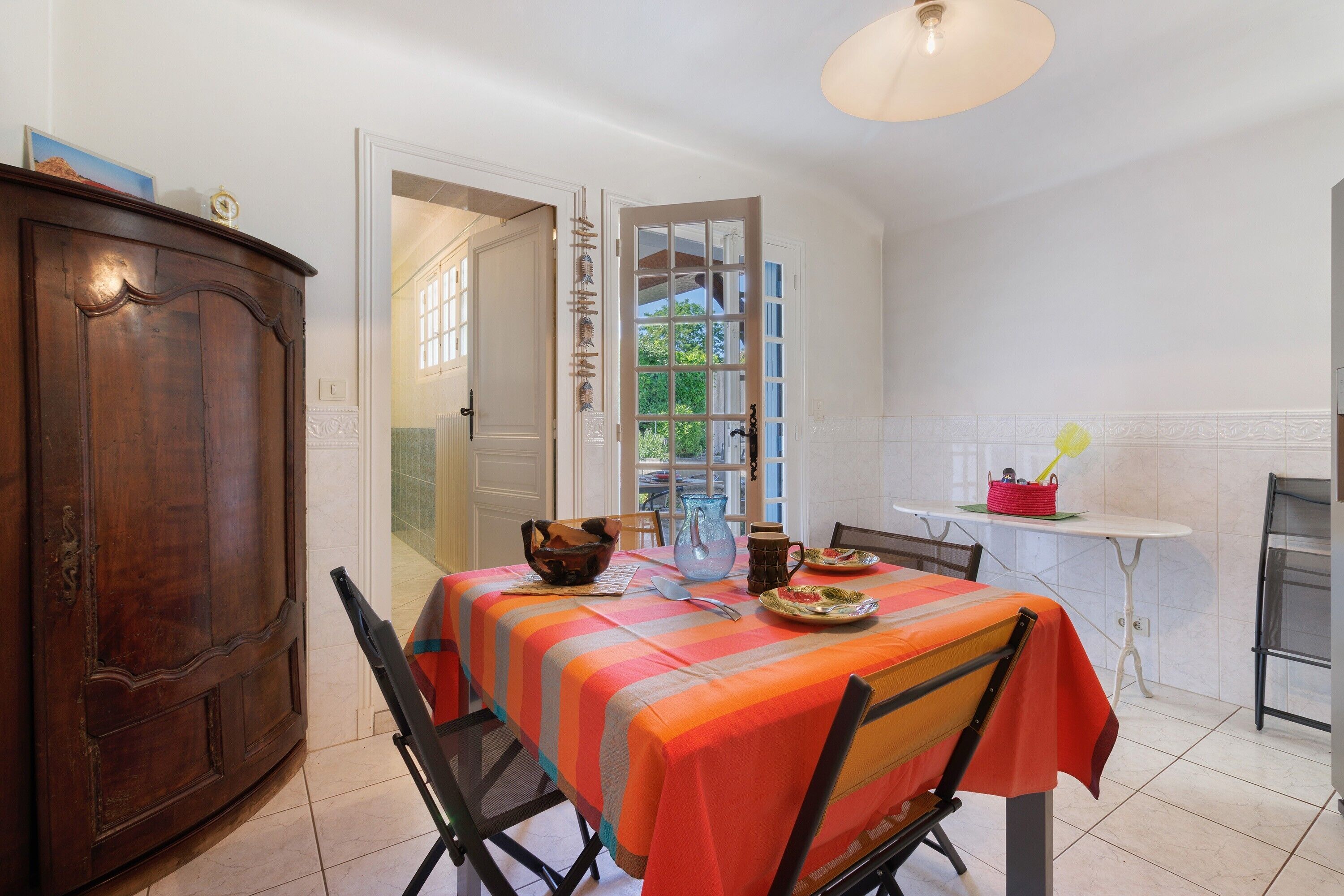 A dining area with a table set for two, a cabinet, and a view through an open door.