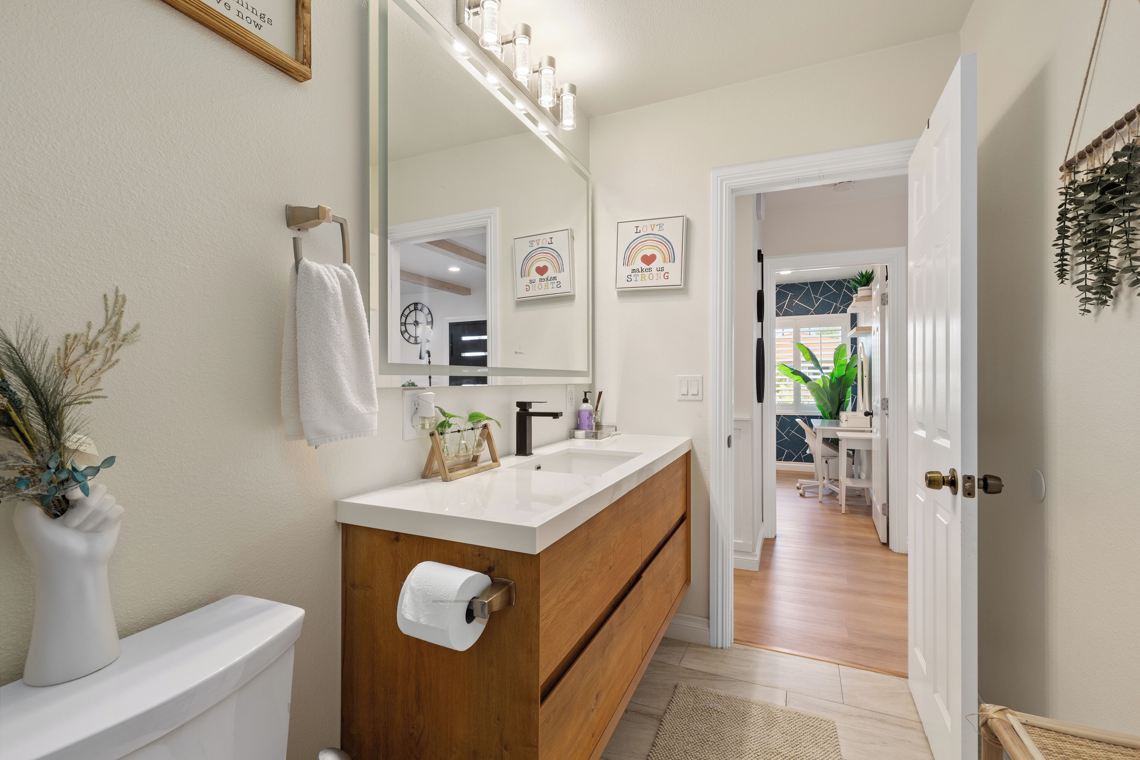 Une salle de bain avec des toilettes blanches, un meuble-lavabo en bois, un miroir et un porte-serviettes.
