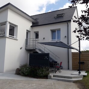 Ein modernes, zweistöckiges Haus mit überdachter Terrasse, einer Treppe und einer kleinen Außenlounge.