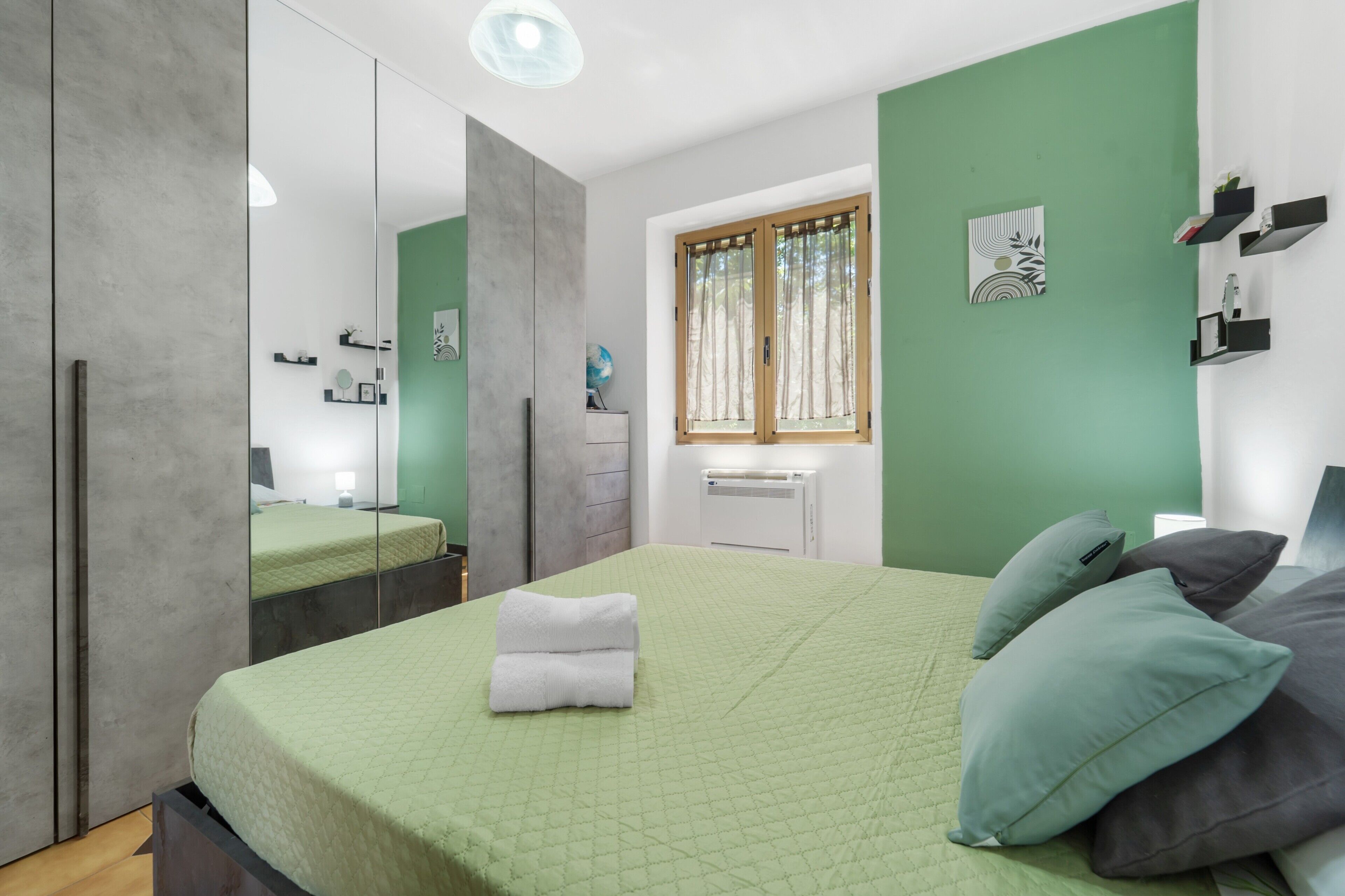 Ein Schlafzimmer mit Bett, Spiegel, Fenster und Heizkörper.