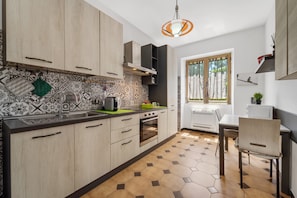 Una cocina moderna con armarios de madera, un salpicadero con diseño, una zona de comedor con mesa y sillas, y un ventanal con vistas a árboles.