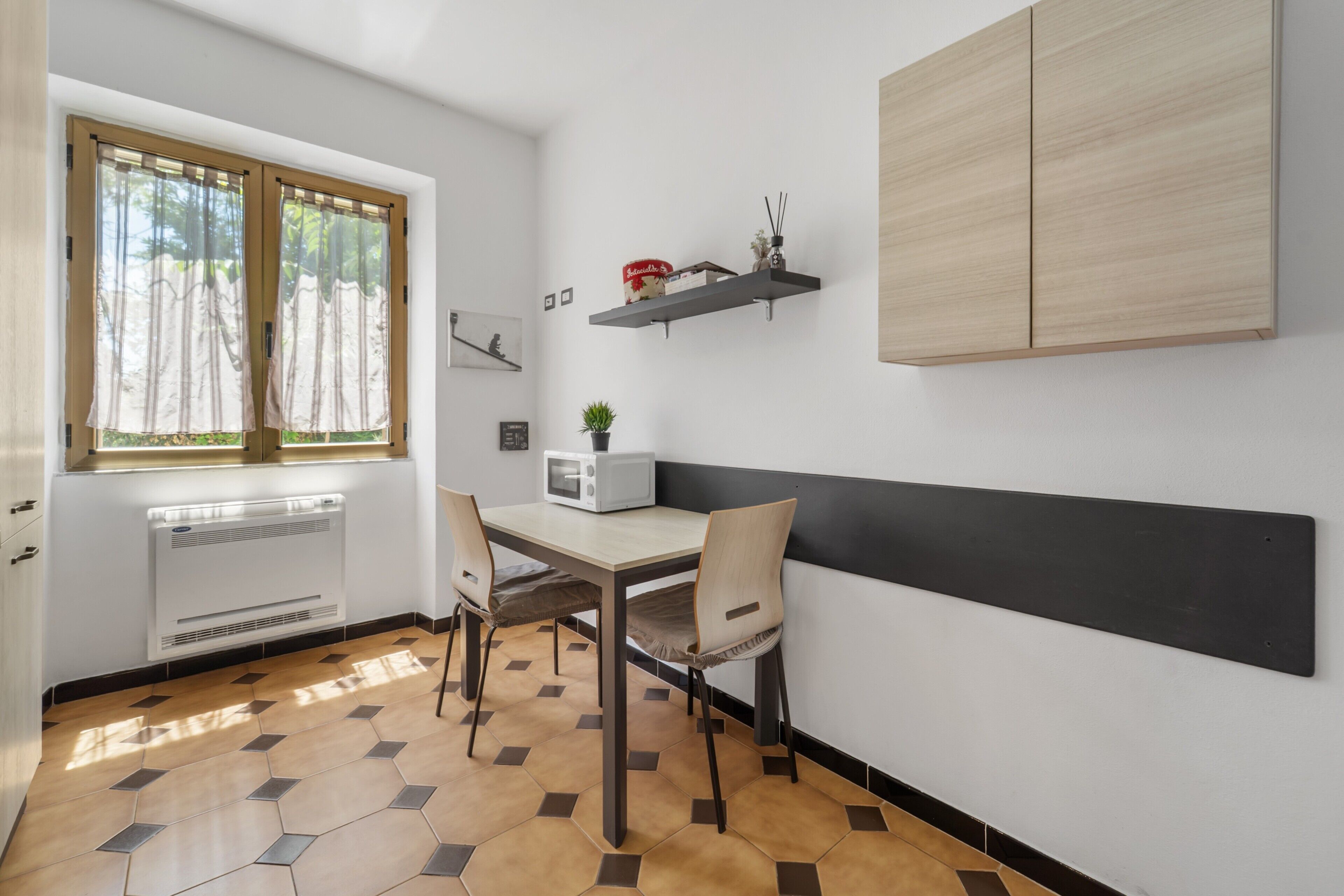 A kitchen with a window, a microwave, a table, chairs, and a shelf with items.