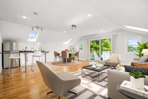 Ein modernes Interieur mit Küche, Essbereich und Wohnzimmer, ausgestattet mit einem Oberlicht, großen Fenstern und Blick ins Freie.
