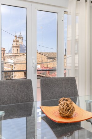 Ein Zimmer mit Glastisch, zwei Stühlen, einer Dekorationskugel und Blick auf ein historisches Gebäude durch ein Fenster.