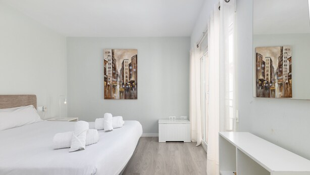 Moderni hotellihuone, jossa on suuri sänky, yöpöytä, pieni sivupöytä, valkoinen penkki ja suuri peili.