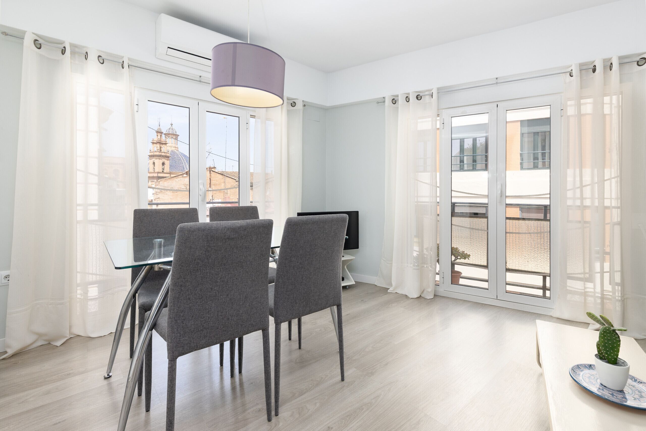 A modern room with a dining table, chairs, a television, and large windows with curtains.