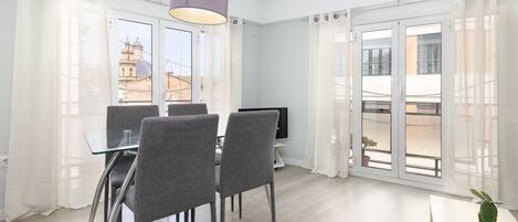 A modern room with a dining table, chairs, a television, and large windows with curtains.