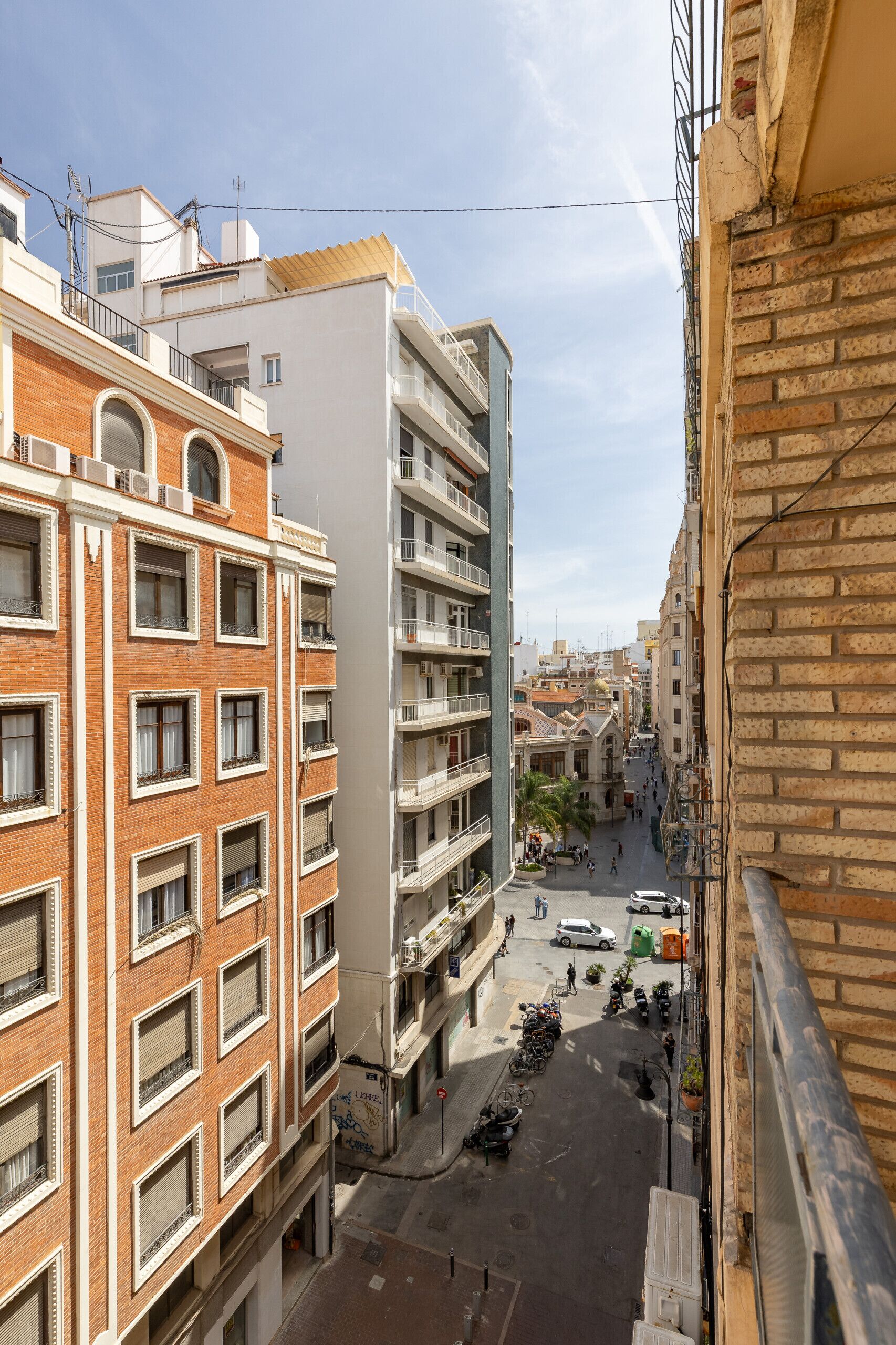 A multi-story building with balconies, a street in front, and a clear sky.