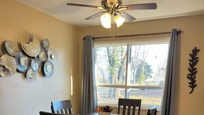 A dining area with a table, chairs, a ceiling fan, and a window with curtains.
